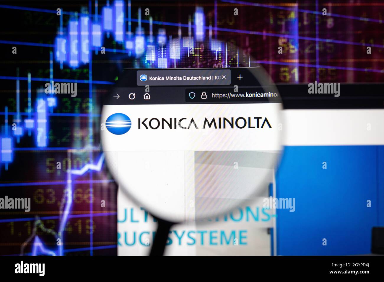 Konica Minolta company logo on a website with blurry stock market graphs in the background, seen on a computer screen through a magnifying glass. Stock Photo