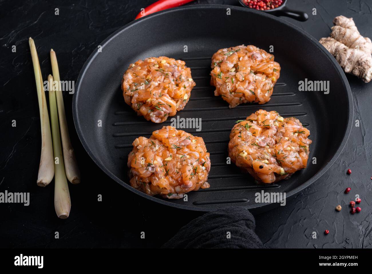 Raw fish patties with salmon fillet and lemongrass, on black textured ...
