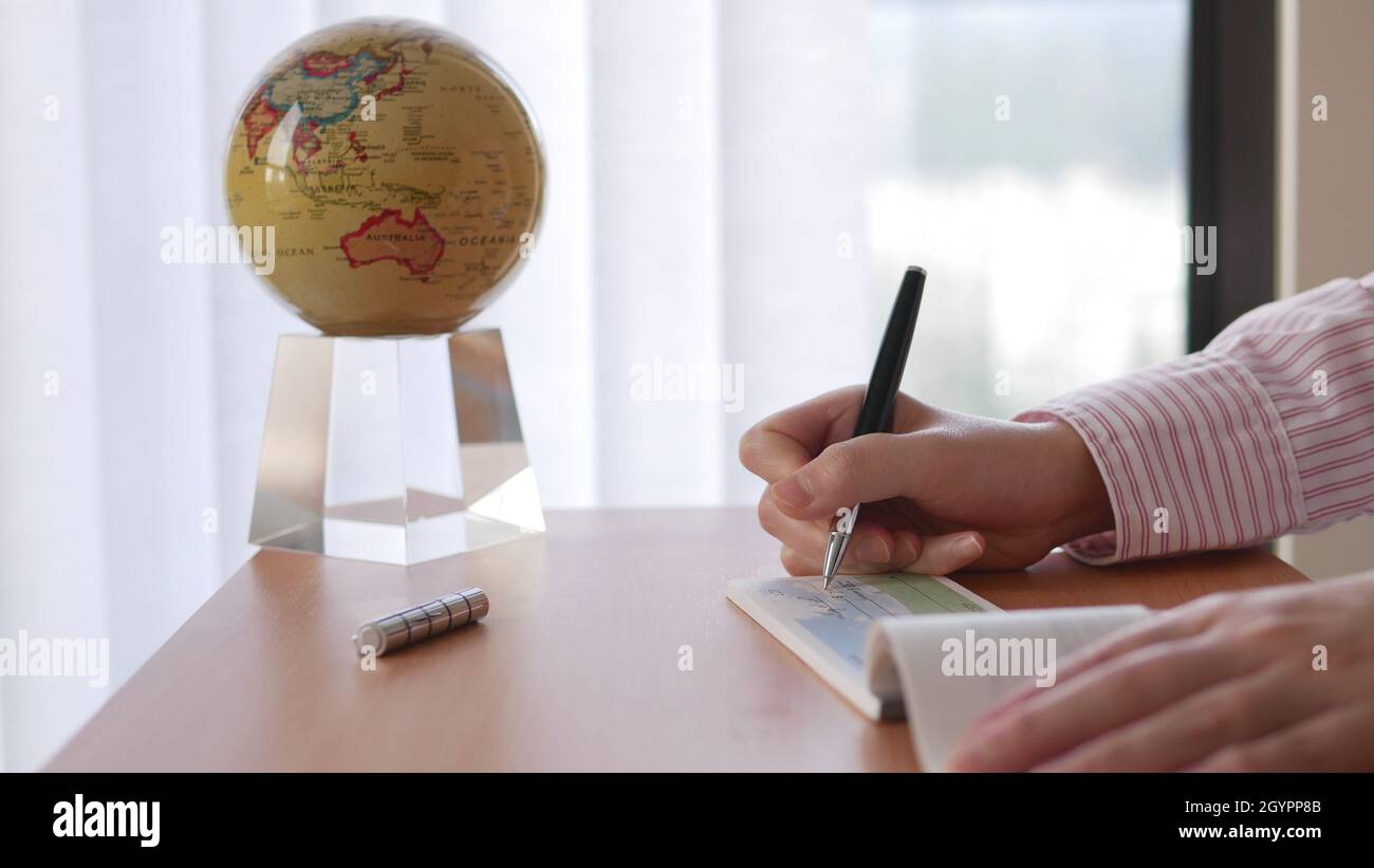 Close up of businesswoman writing a check with globe spinning inside the office Stock Photo