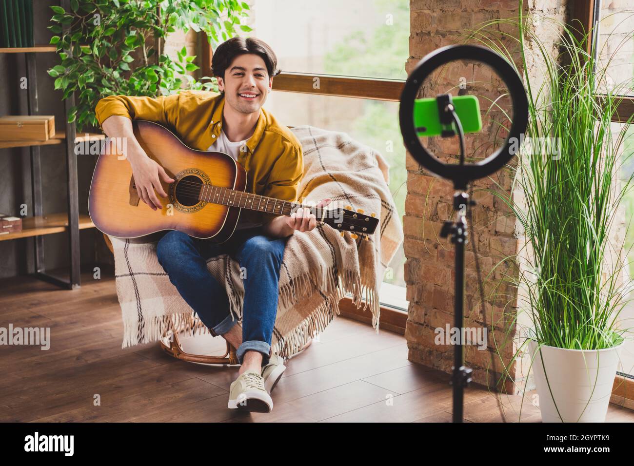 Photo of blogger musician guy sit armchair play guitar make performance  live video wear yellow shirt home indoors Stock Photo - Alamy