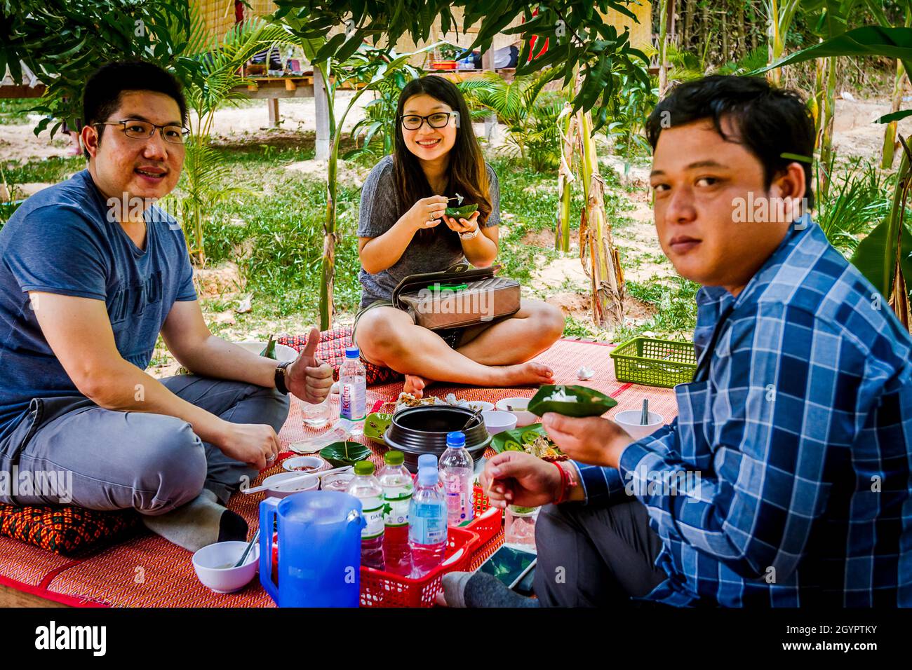 Group of Cambodians eating on the ground a family style meal showing a tourist their culture. Stock Photo