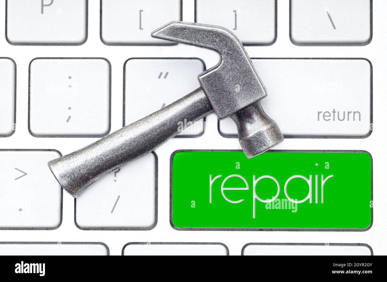 Small steel hammer lies on the keyboard, which has a green key labeled REPAIR. Hardware service concept. Stock Photo