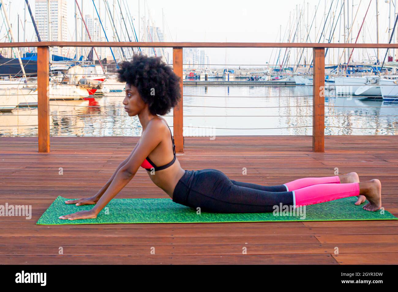 Young athletic woman in sports clothes stretching on a mat on a wooden deck in a marina Stock Photo