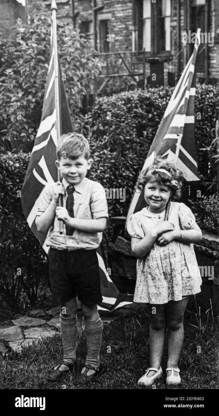 Young children proudly hold flags of the United Kingdom to mark the Coronation of the British monarch, King George VI, on 12 May 1937 Stock Photo