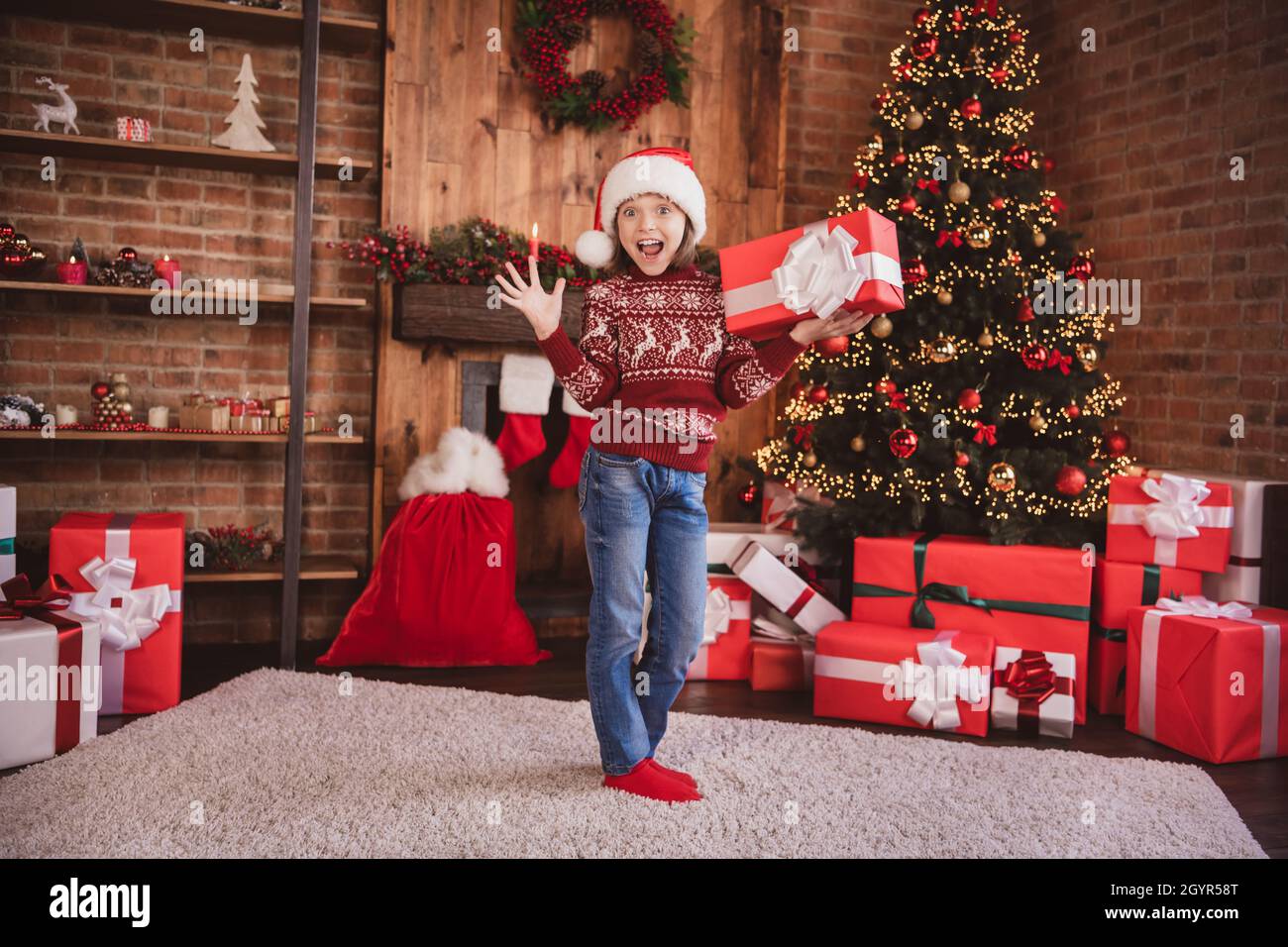 Photo of excited crazy shocked impressed little girl hold giftbox wear pullover santa headwear socks indoors Stock Photo
