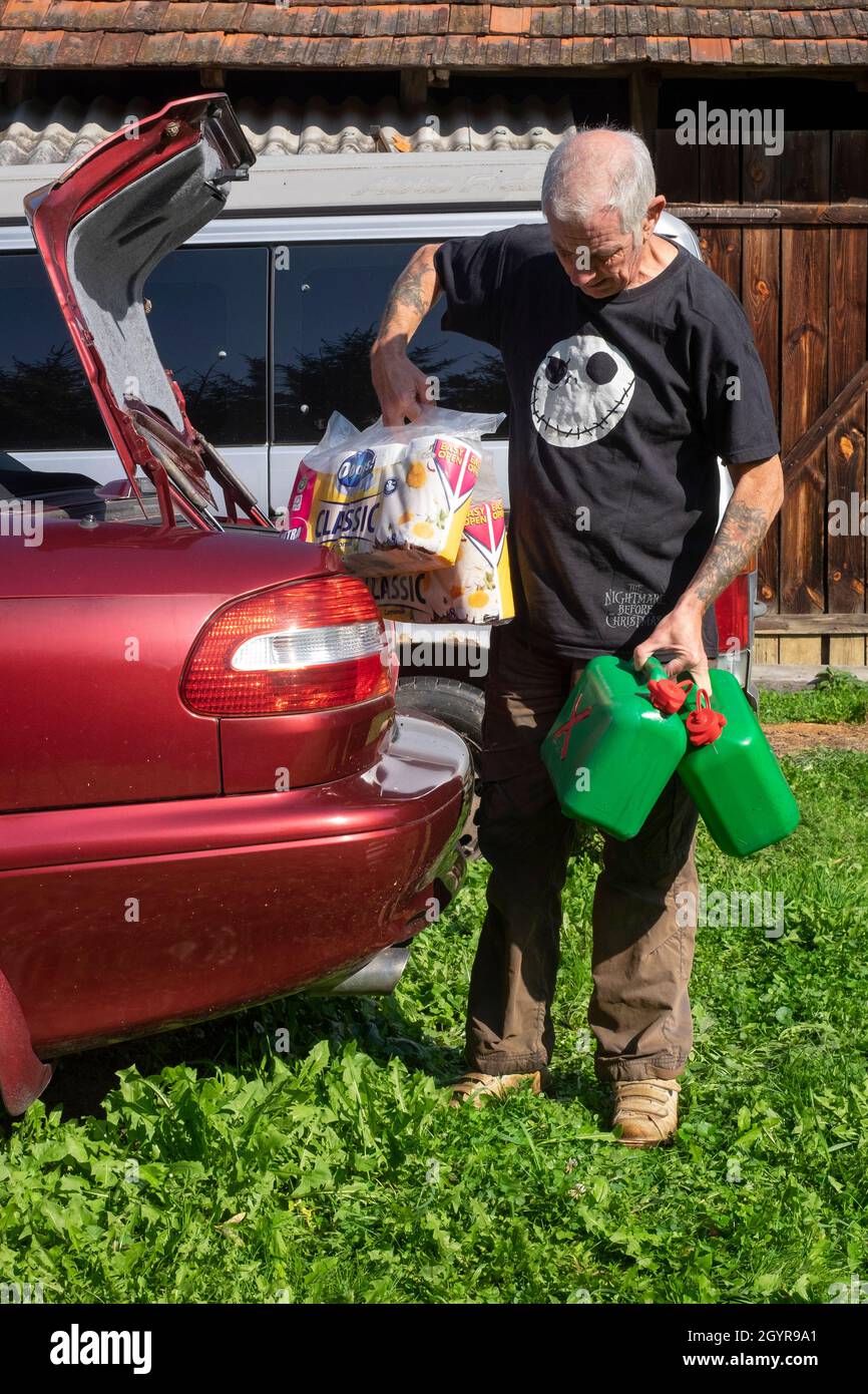 older man wearing nightmare before christmas t shirt unloading car boot  full of petrol containers and multi packs of toilet roll Stock Photo - Alamy