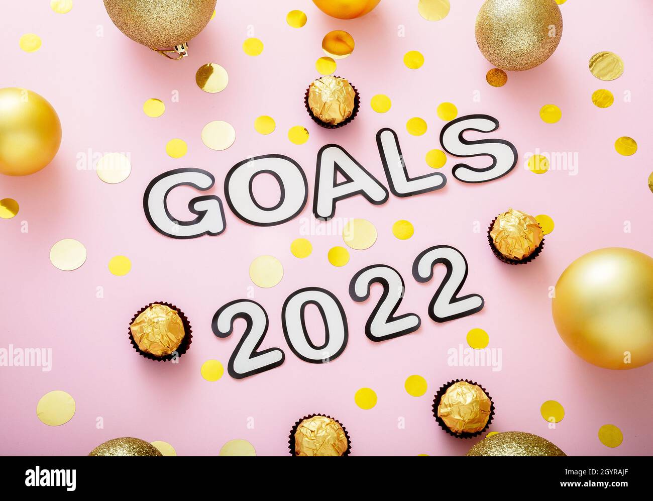 2022 Goals text with Christmas decorations gold confetti on pink color background. Goals 2022 lettering in Happy New Year style Stock Photo