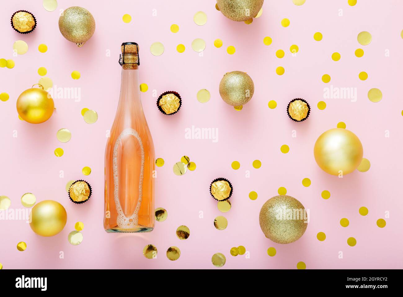Pink champagne bottle with confetti, sweet candies and Christmas balls golden christmas decorations on pink background. Flat lay Stock Photo