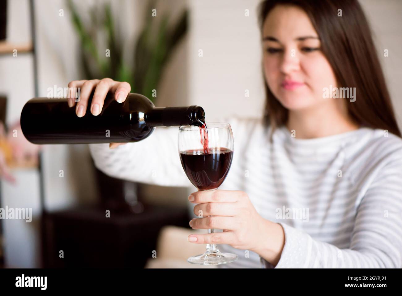 Pregnant alcoholic woman is pouring wine from a bottle into a glass and