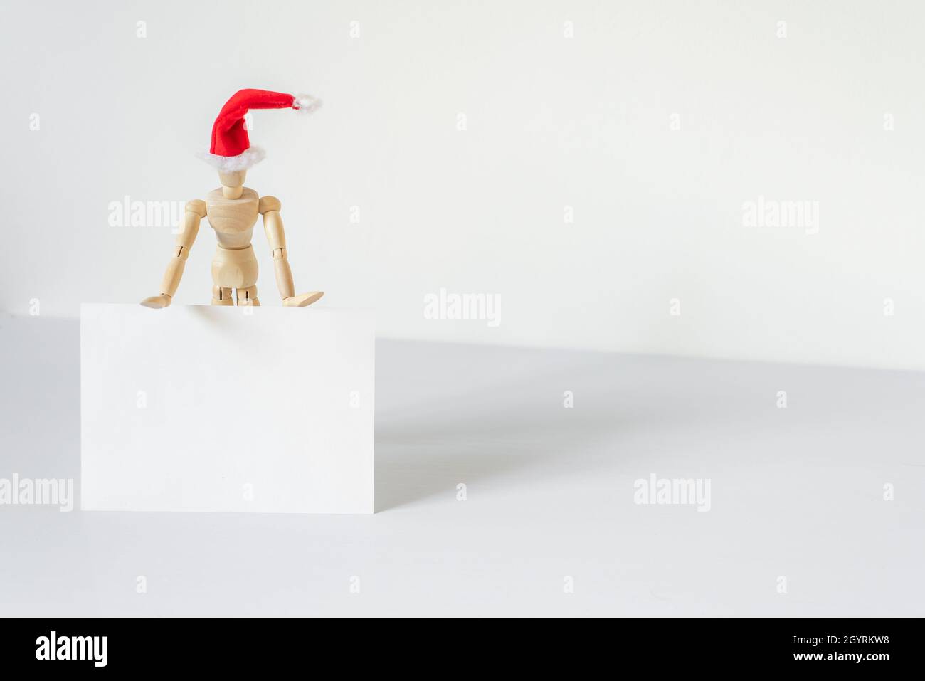 Christmas blank greeting card mock-up scene. Wooden mannequin posing on greeting card or gift list with red Santa Claus hat.Modern and minimal Santa C Stock Photo