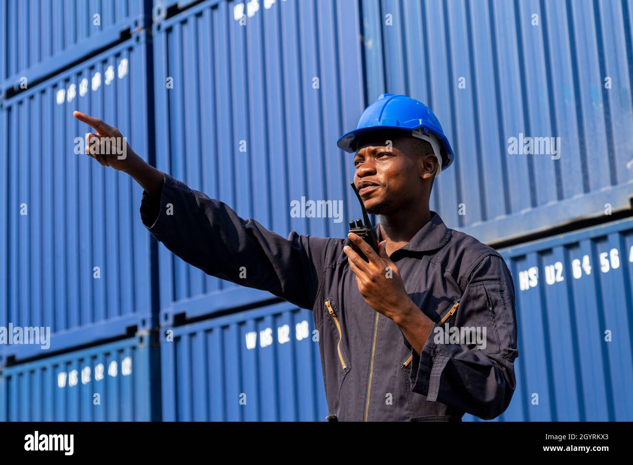black african amarican man worker working control loading freight containers at commercial shipping dock. cargo freight dock and import export logistic Stock Photo