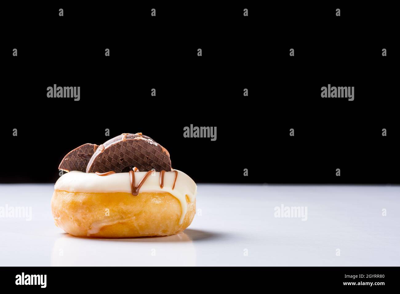 Photograph of a white chocolate donuts with dark chocolate cookies on a white table and a black background.The photo is taken in horizontal format and Stock Photo