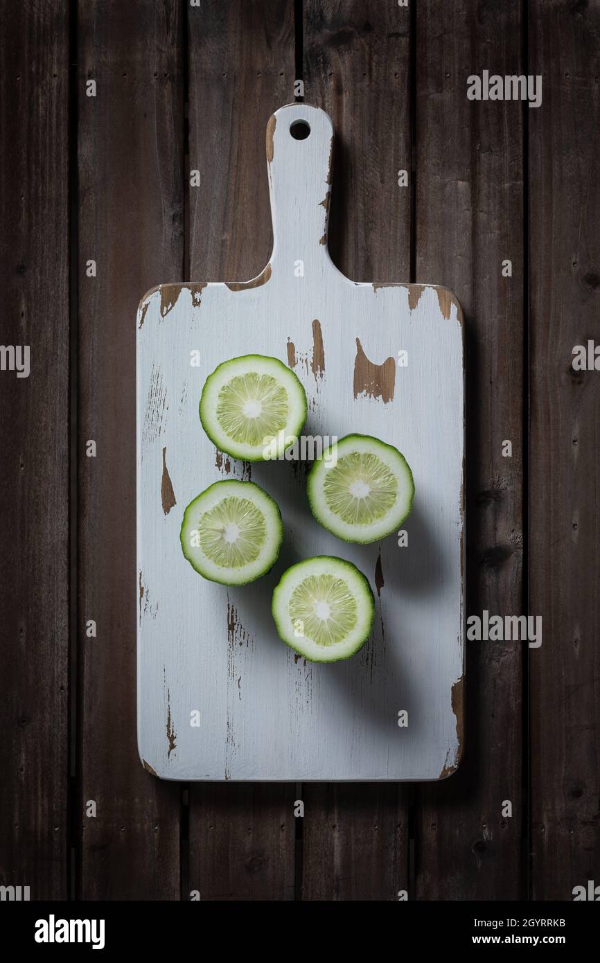 Cut green lemon on white wooden cutting board. Stock Photo