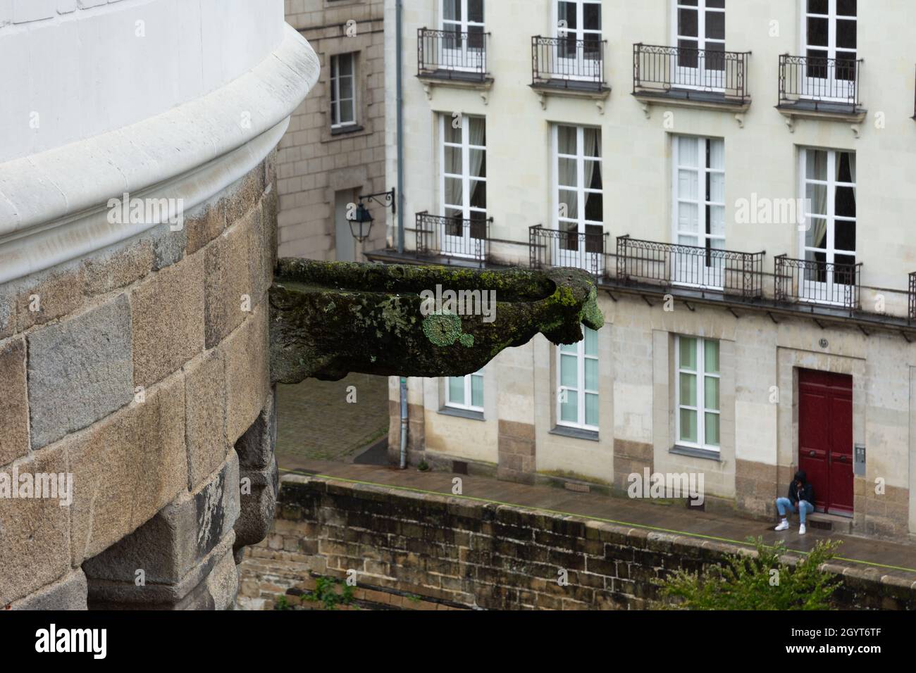 Gargoyle-shaped umbrella stand in the form of a castle looking down on a young immigrant in a hoodie cowering in the cold, sitting on the sidewalk. So Stock Photo