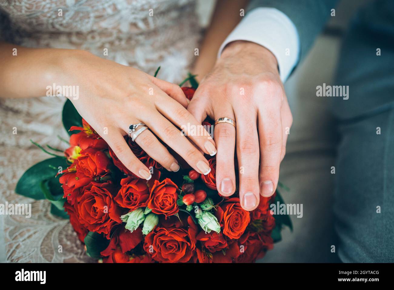 couple hands with rings on the wedding bouquet with red roses white