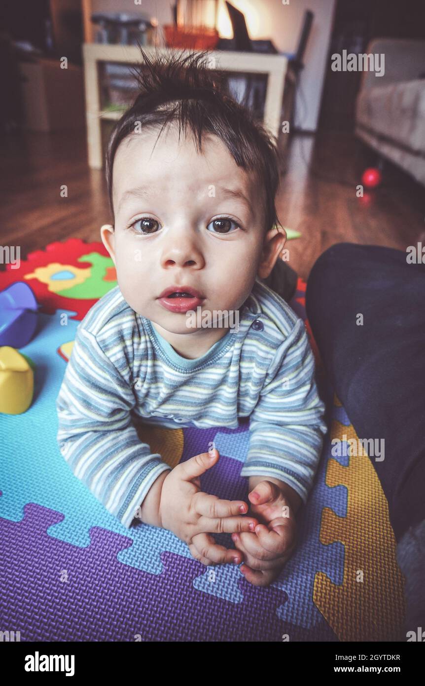 Cute adorable Caucasian kid lying on the kid carpet and looking at the