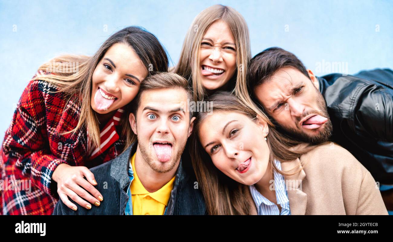 Multicultural milenial guys and girls taking selfie sticking out tongue with happy faces - Crazy life style concept with young students friends having Stock Photo