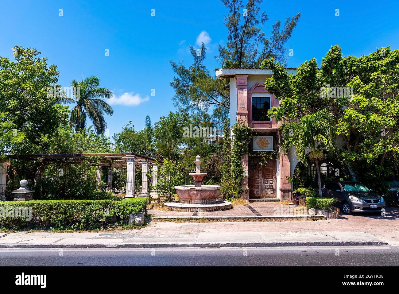 Rustic abandoned Spanish style residential bungalow and fountain beside road Stock Photo