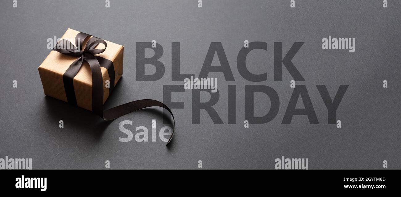 Black Friday Sale text lettering and a gift box with a ribbon bow, dark background. Special seasonal offers sign, banner Stock Photo