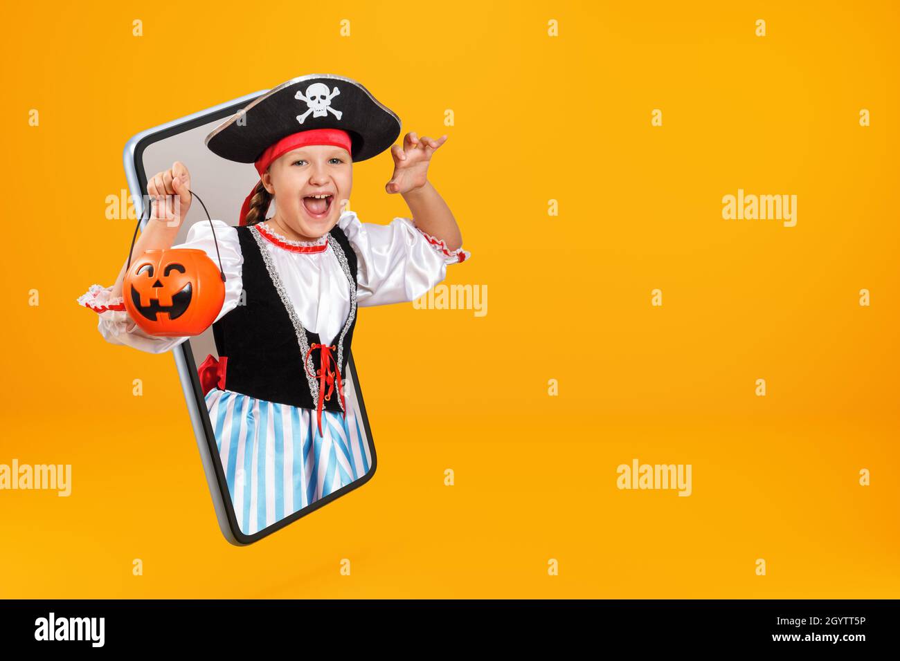 A little girl dressed as a pirate for Halloween is holding a pumpkin lantern bucket with a frightening expression on her face. Child online on the sma Stock Photo