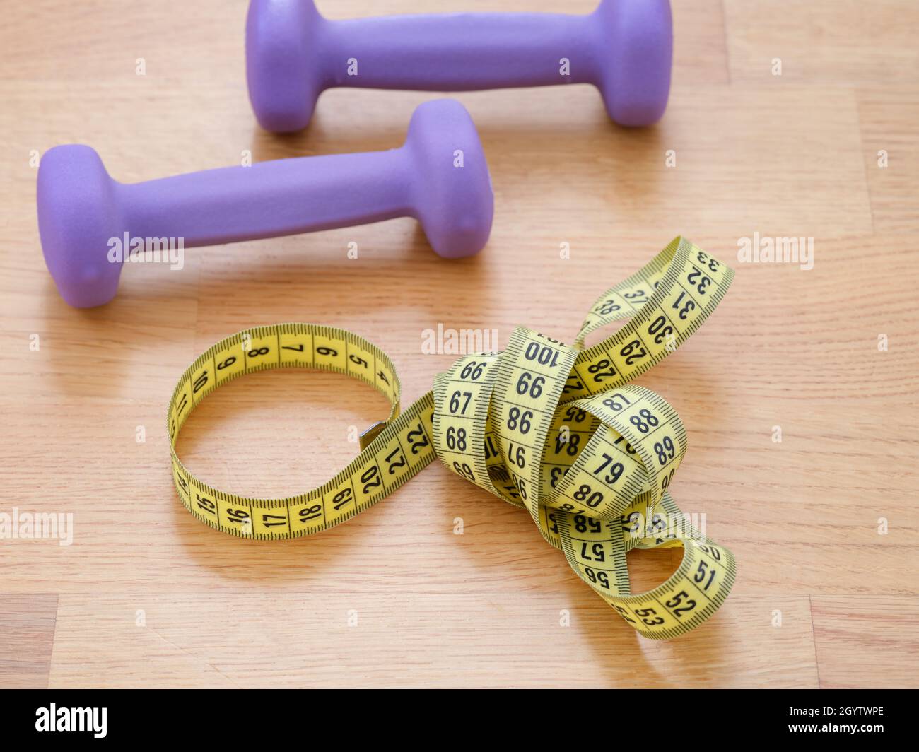 A tape measure and dumbbells lying on the floor. Close up. Stock Photo