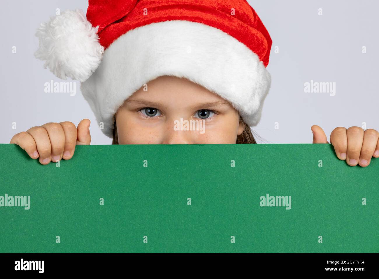 close-up portrait of a girl in a Christmas gnome hat hiding behind a black green poster in her hands , isolated on a white background Stock Photo