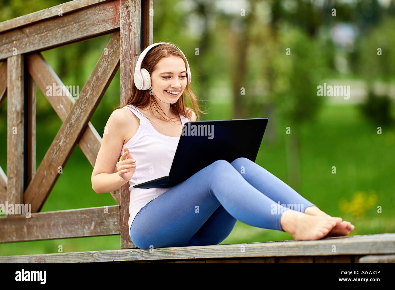 Remote work by happy white woman in headphones with laptop outdoors. Stock Photo