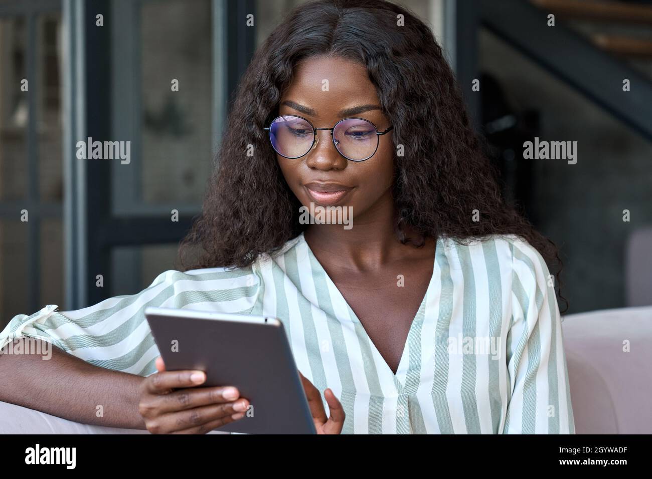 Young black African woman holding using digital tablet sitting on couch at home. Stock Photo