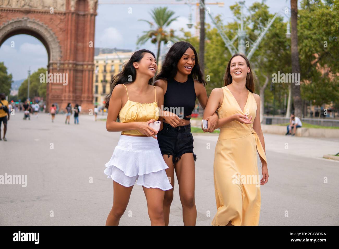 Positive multiracial young fashionable women in summer outfits talking and laughing happily while walking together on street of Barcelona city Stock Photo