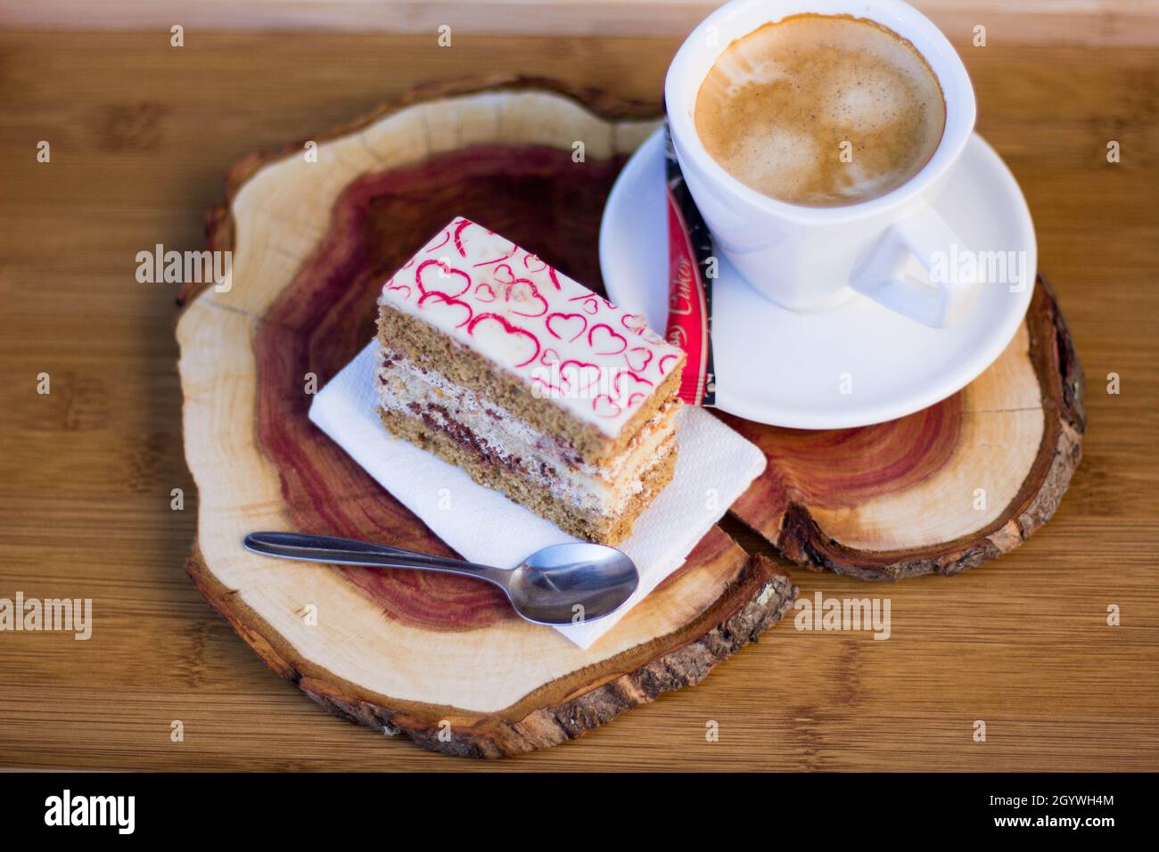 Tasty Slice of Cake with Cream Filling and Heart Decor on Top with Coffee on Cherry Board. Coffee Break Stock Photo