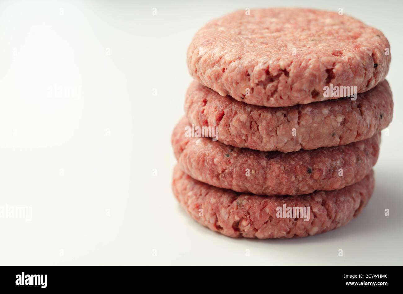 Raw beef burgers with a pinch of salt and black pepper on the white