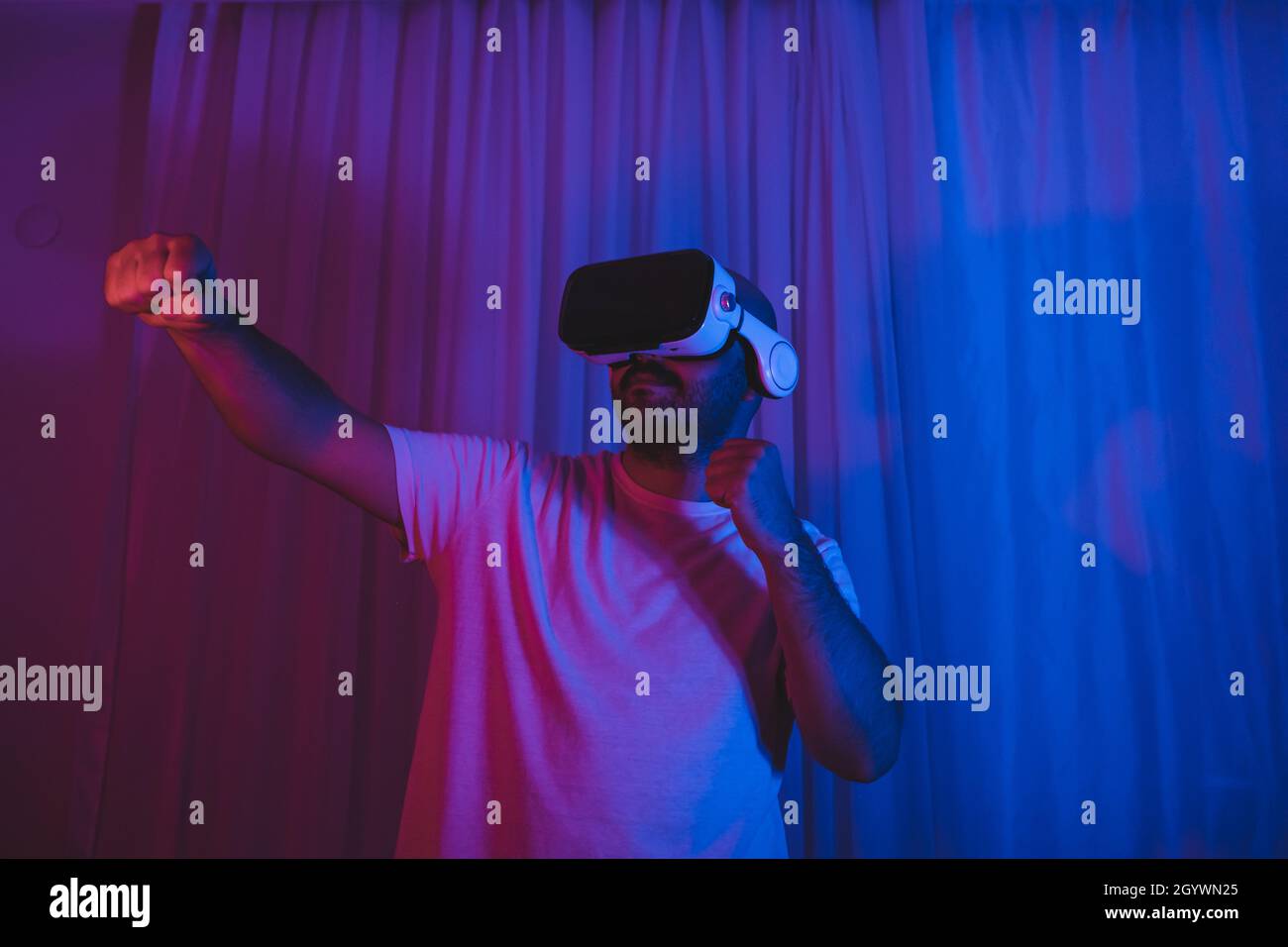 The man who entered the world of the metaverse with VR glasses is playing a boxing match. Young man having sporting fun in the virtual world. Stock Photo