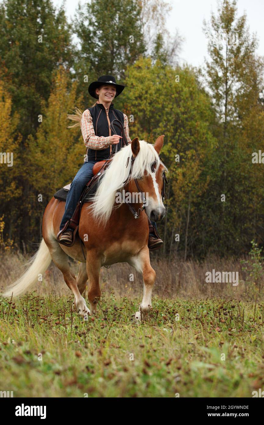 Beautiful cowgirl ride her horse in autumn country road at sunset Stock Photo