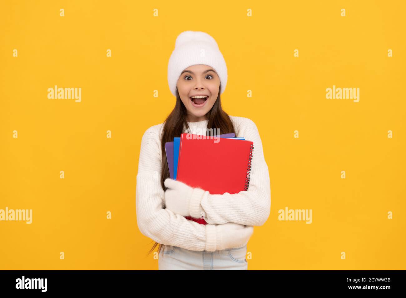 amazed child in winter hat and gloves. back to school. kid with workbook on yellow background. Stock Photo