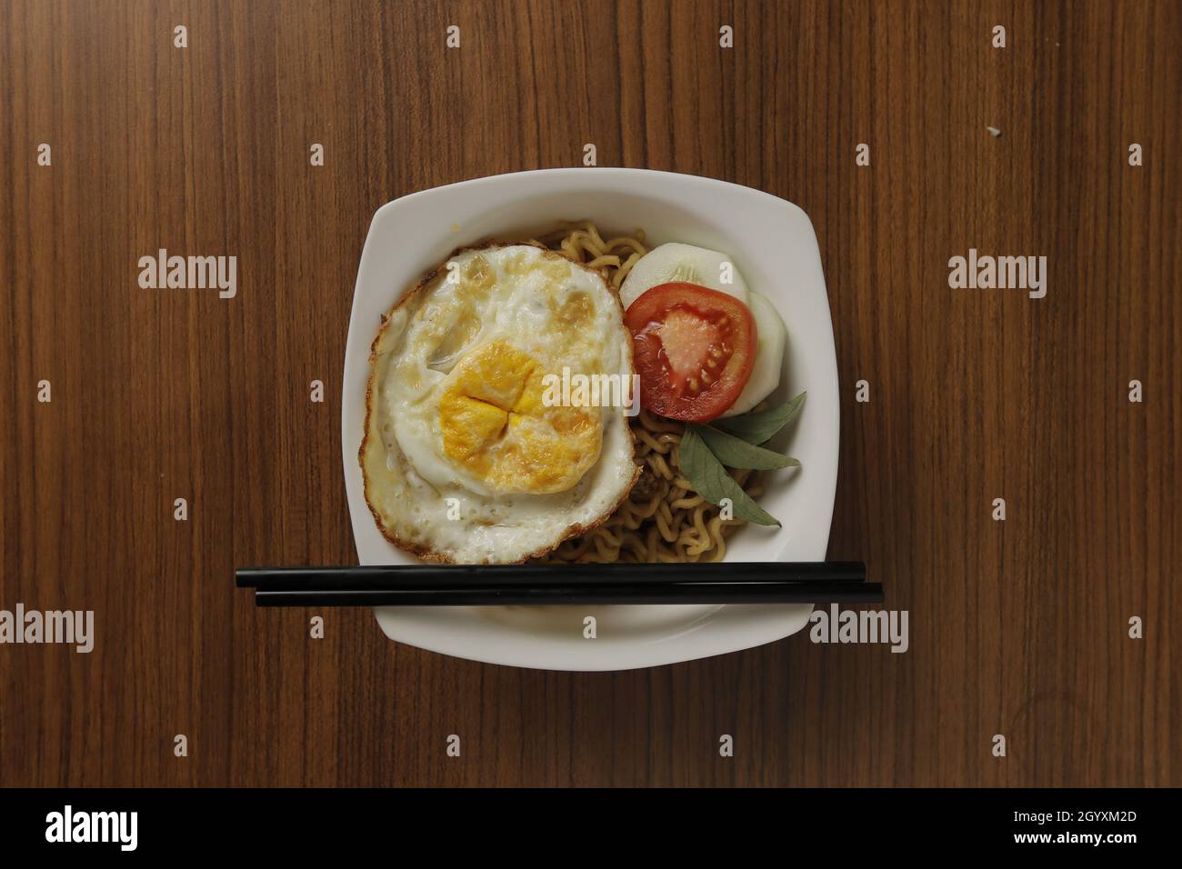 Fried noodles, eggs, tomatoes, and cucumbers as accompaniments placed on a wooden table. Stock Photo