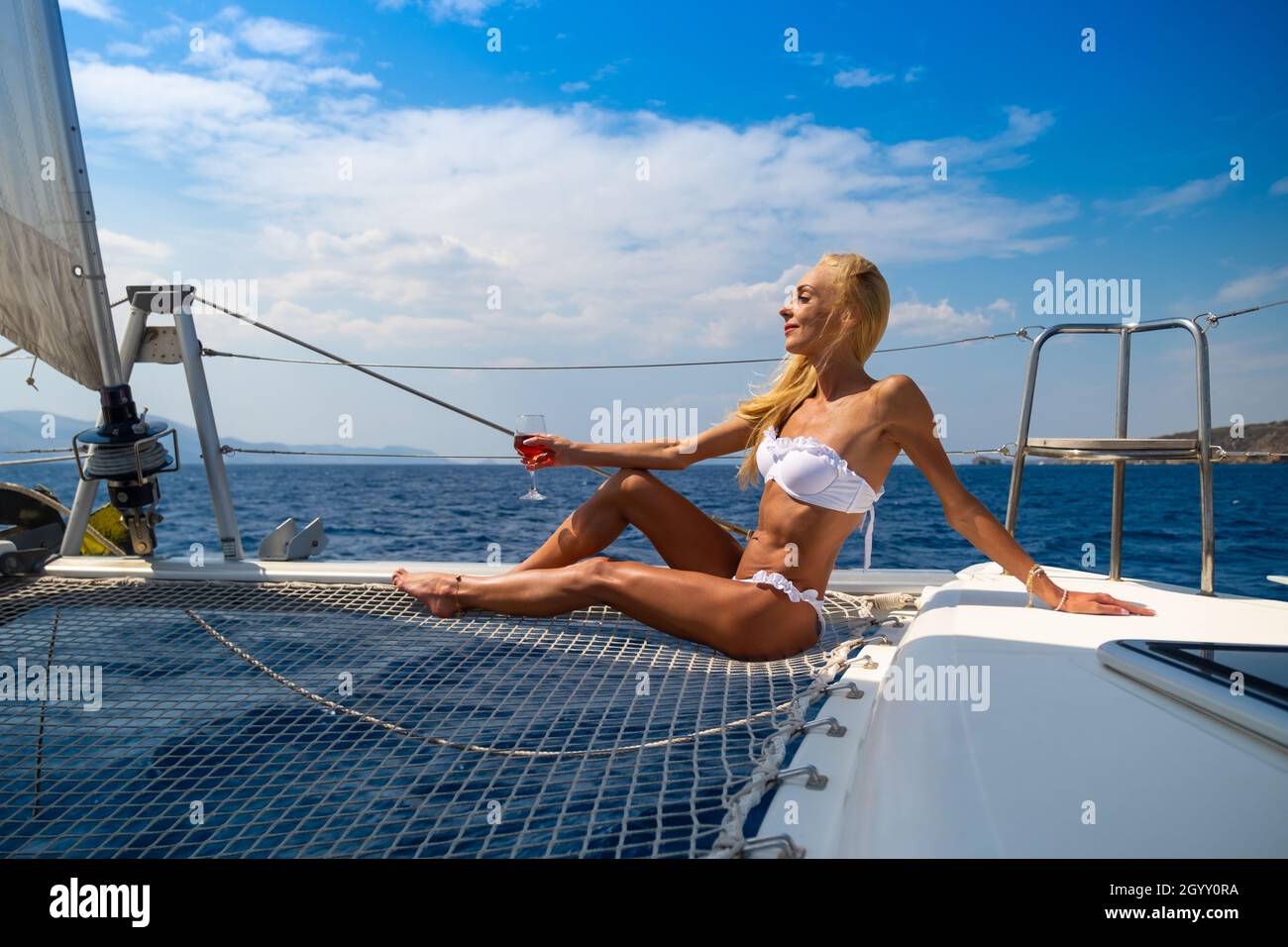 Woman in bikini tanning and relaxing drinking wine on a summer catamaran sailing cruise Stock Photo