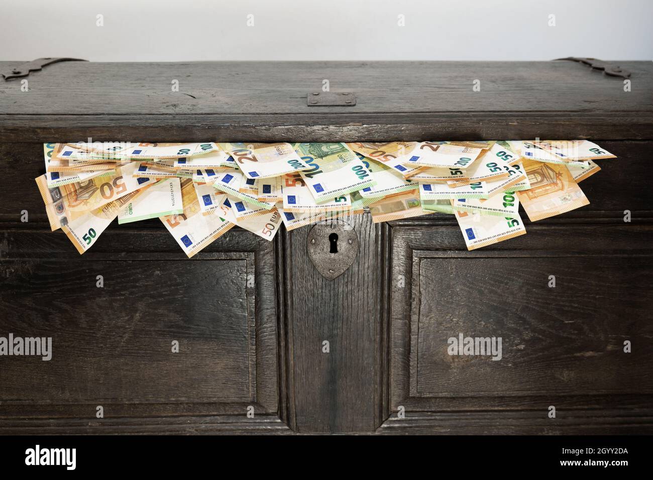 Antique wooden chest from which euro bills spill out. Savings, black money, cash, cash flow. Stock Photo