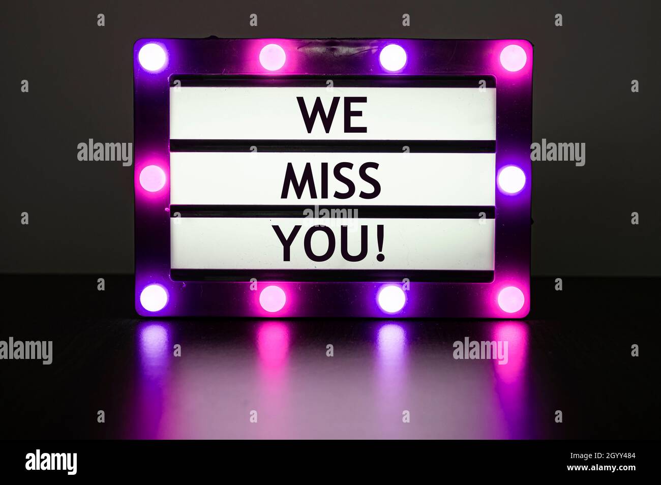 Lightbox with pink lights in dark room with words - we miss you! Stock Photo