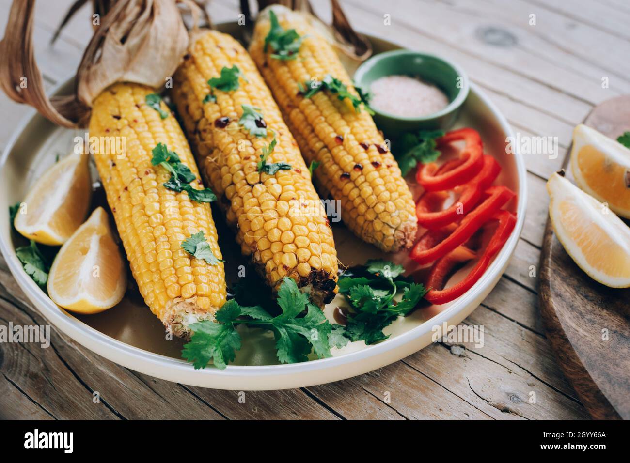 Baked corn cobs with sauce, coriander, sliced bell pepper, lemon and
