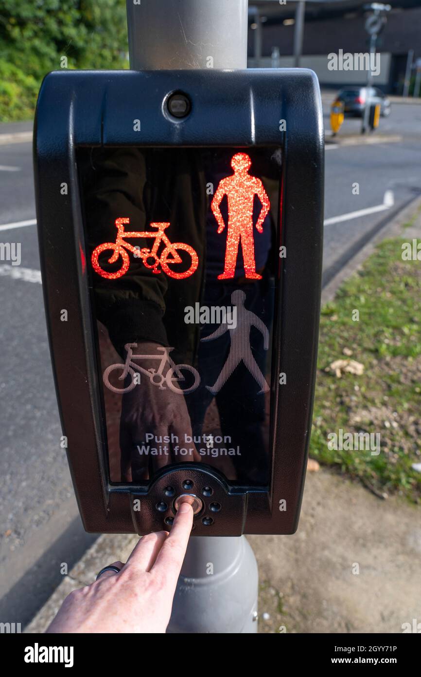 A man's finger pushing a button on a pedestrian crossing signal on red man 'Do Not Cross' next to a busy road in Basingstoke, UK Stock Photo