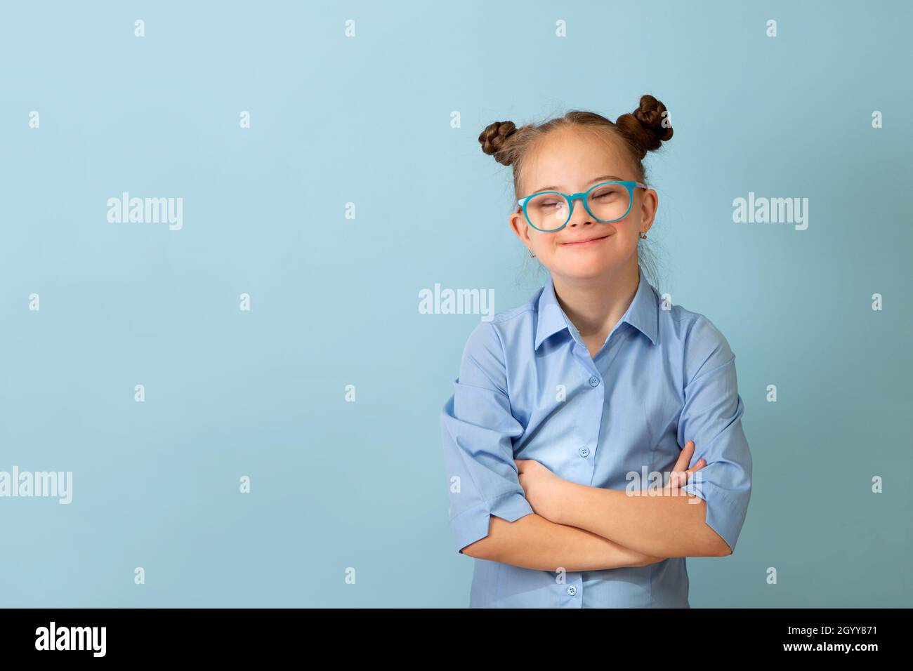 Happy girl with Down syndrome. Having fun, laughing. Funny pigtails. Studio. Portrait on a blue background Stock Photo