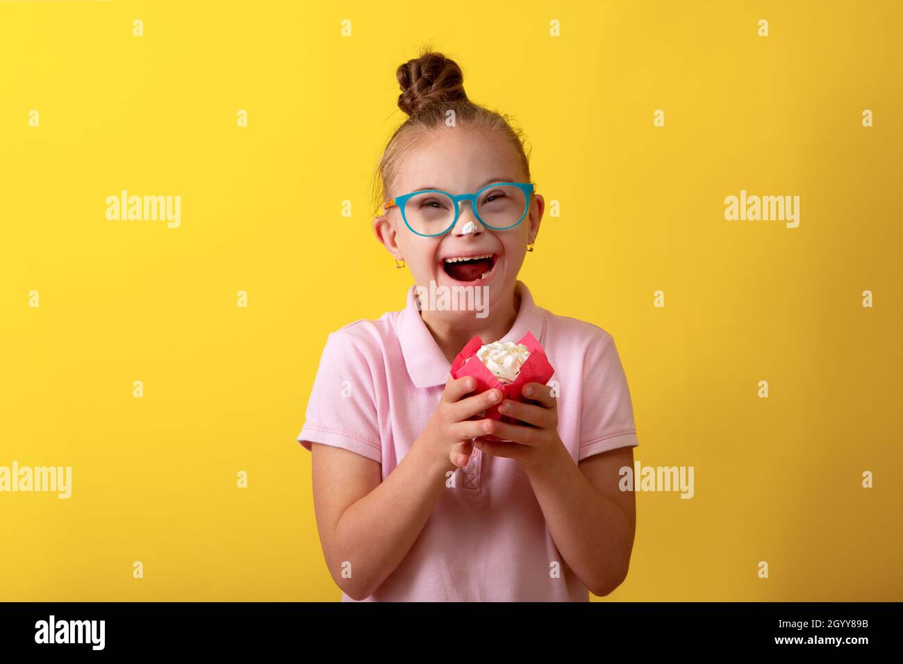 Happy girl with Down syndrome. Having fun, laughing. Funny pigtails. Studio. Portrait on a yellow background. Happy birthday Stock Photo