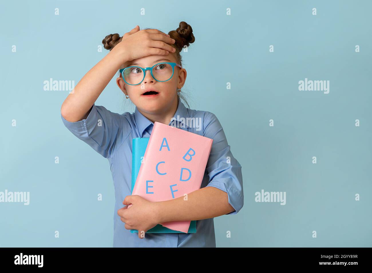 Happy girl with Down syndrome. Having fun, laughing. Funny pigtails. Studio. Portrait on a blue background. Back to school Stock Photo