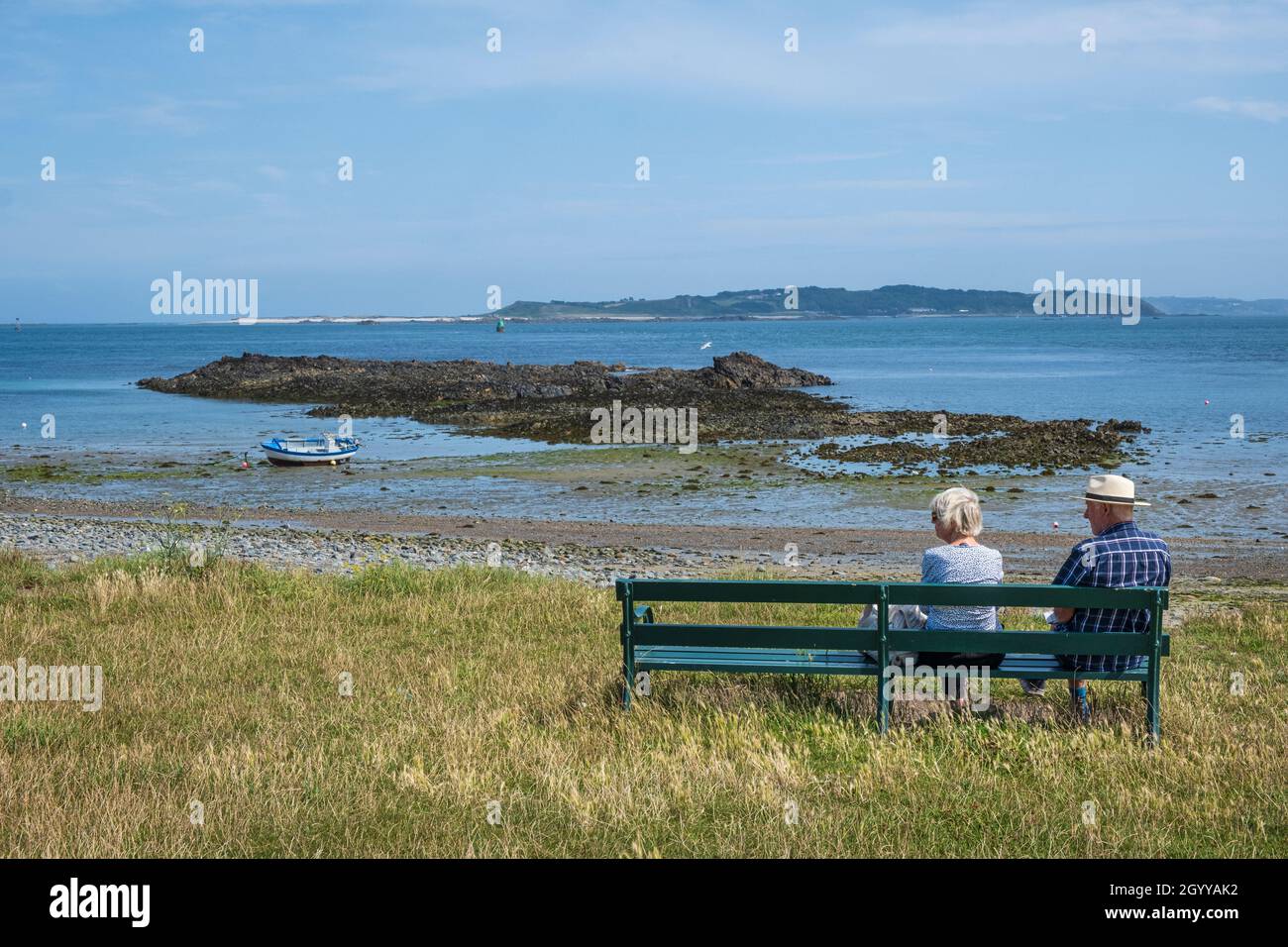 Couple sitting on a bench at Vale with a view towards Herm Island, Guernsey, Channel Islands Stock Photo