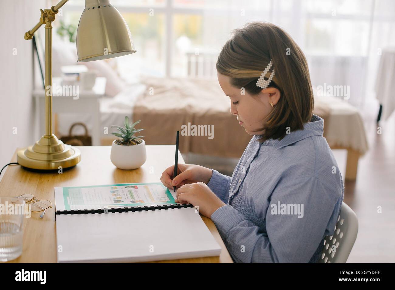 Young girl studying at home writing notes sitting at desk. Concept of home schooling, distance education concept Stock Photo