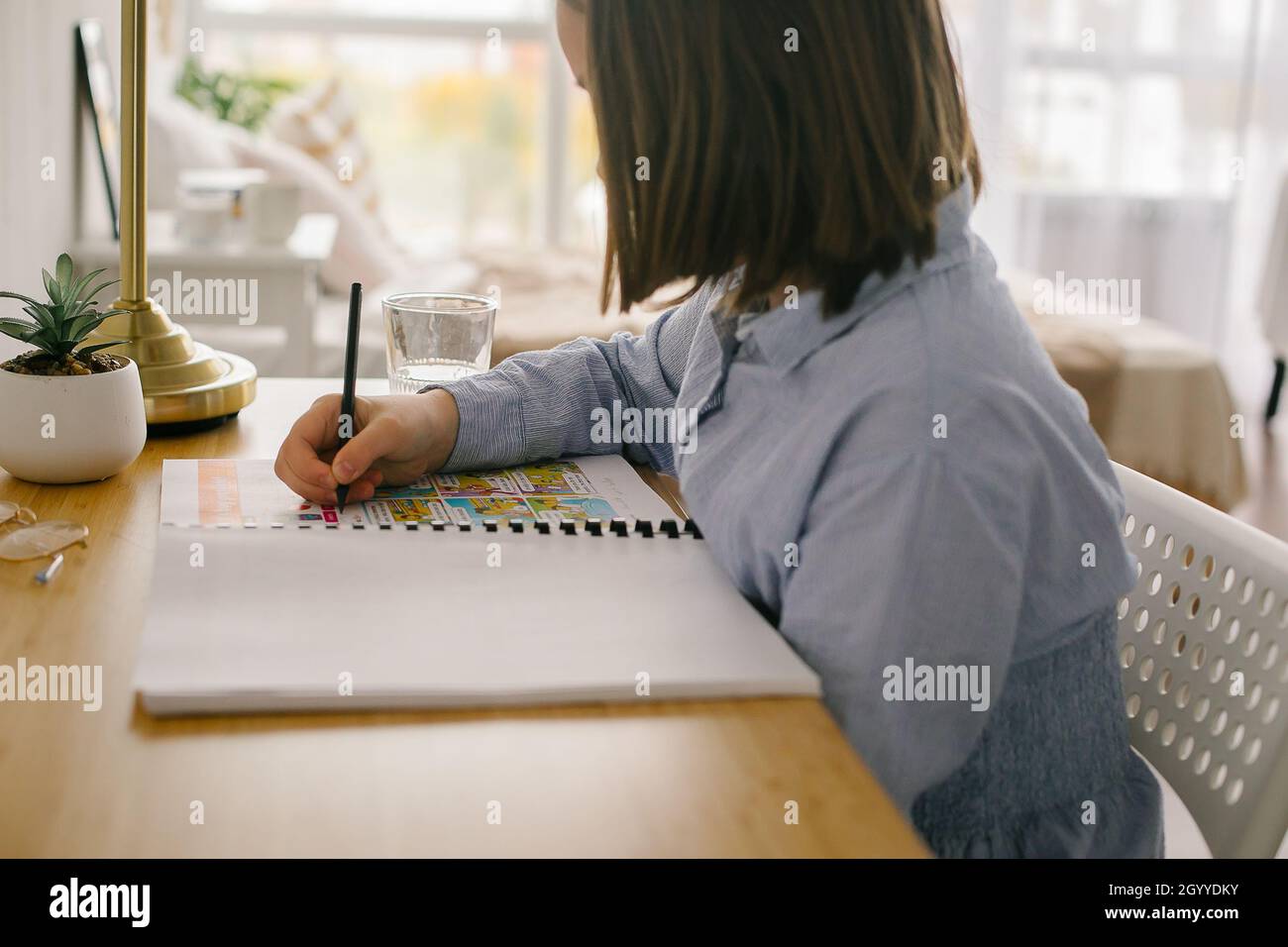 Young girl studying at home writing notes sitting at desk. Concept of home schooling, distance education concept Stock Photo