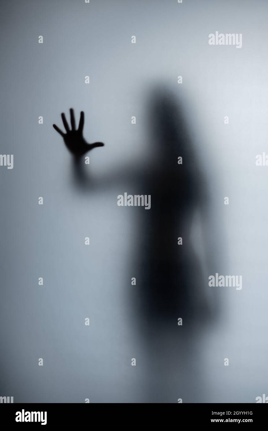 Possessed woman scratching glass with hands, creepy female silhouette, horror. Scary ghostly creature behind the glass. Stock Photo