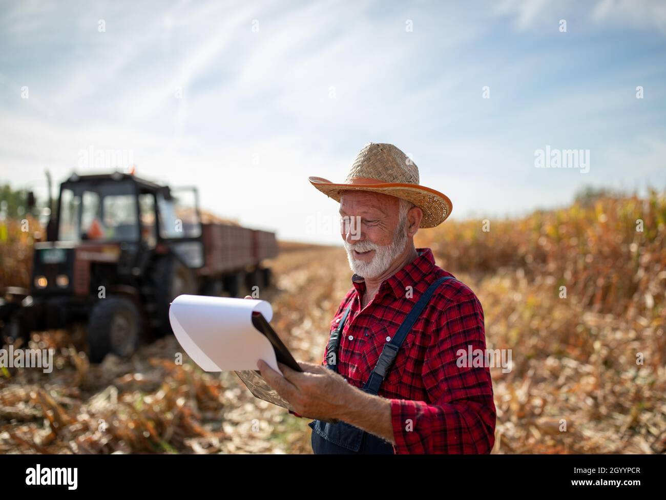 Senior farmer with straw hat holding note book and standing in front of ...