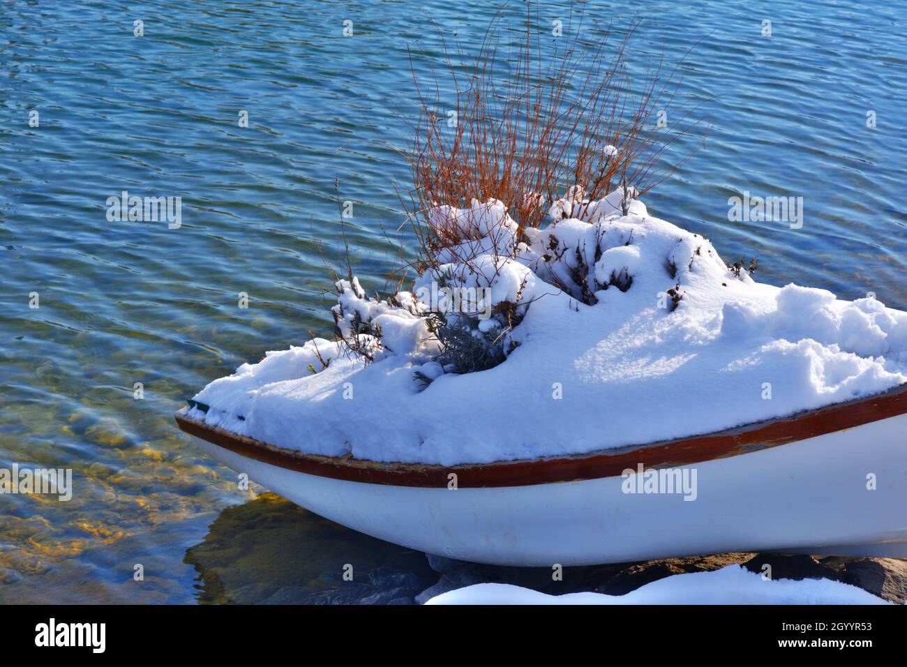 Small wooden rowing boat at lakeside under snow in winter Stock Photo