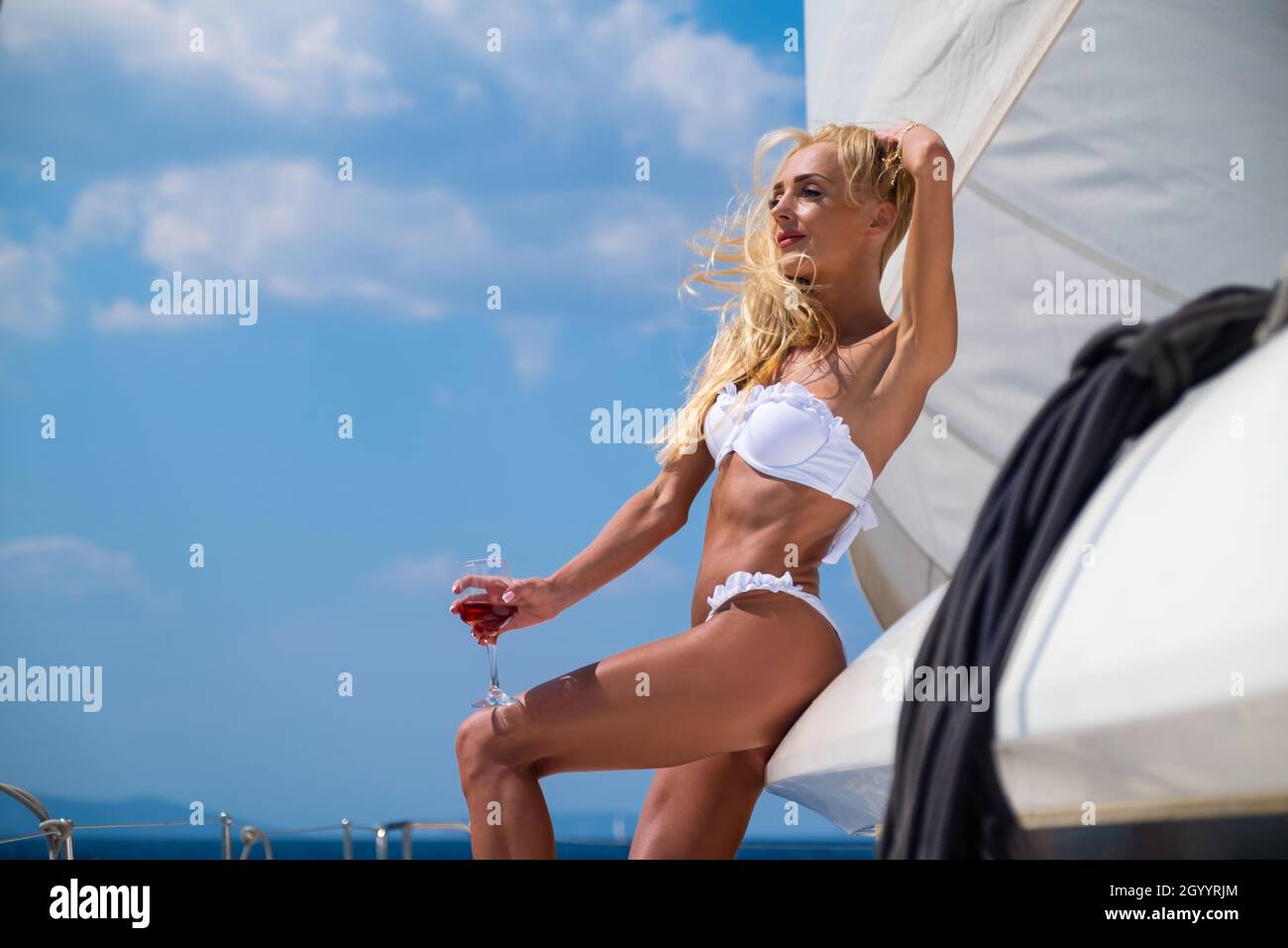 Woman in bikini tanning and relaxing drinking wine on a summer catamaran sailing cruise Stock Photo